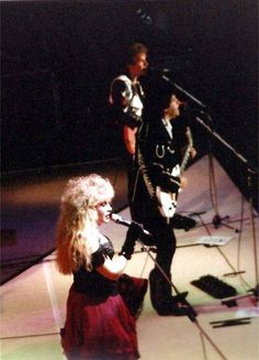 a woman standing next to a man in front of a microphone and guitar on stage