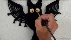 a person holding a pencil in front of a knitted bat with eyes on it