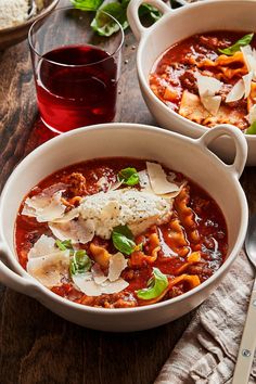 two bowls of pasta and meat soup on a wooden table next to a glass of wine