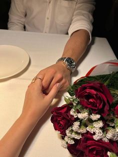 two people holding hands at a table with flowers and plates on the table in front of them