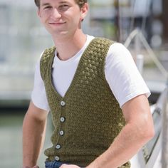 a young man sitting on top of a boat wearing a green knitted sweater vest