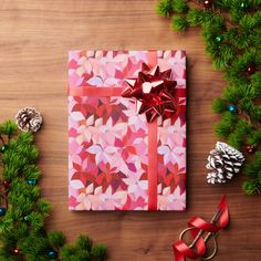 a present wrapped in pink and red paper with a bow on it, surrounded by christmas decorations