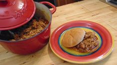 a plate with a hamburger on it next to a pot full of chili and rice