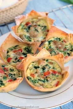 four mini quiches with spinach and cheese on a white plate next to a wicker basket