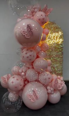 pink balloons are stacked on top of each other in front of a happy birthday sign