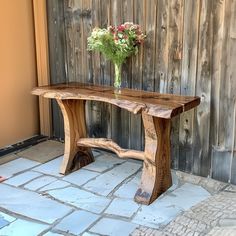 a wooden bench sitting on top of a stone floor next to a flower vase filled with flowers