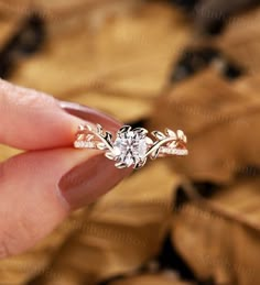 a woman's hand holding an engagement ring with leaves around it and the diamond in the middle