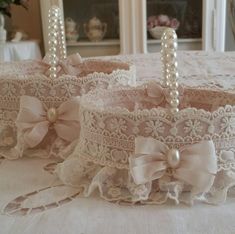 two white lace baskets with bows and pearls on the top are sitting on a table