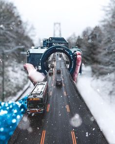 a person holding up a camera on the side of a snow covered road with trees in the background