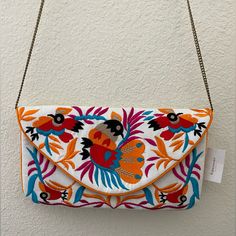 an orange and blue embroidered clutch bag hanging from a chain on a white wall with a tag attached to it