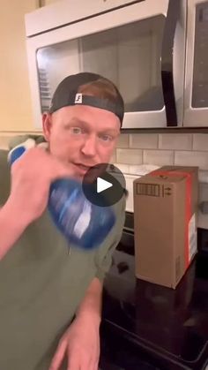 a man in a green shirt and black cap is holding a blue bottle while standing in front of an open microwave