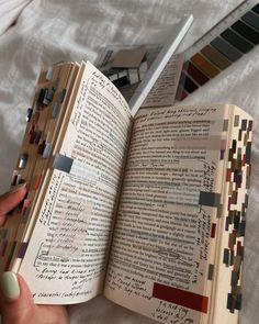 a person is holding an open book on a bed with white sheets and colorful swatches