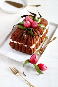 a piece of cake on a white plate with pink tulips and greenery