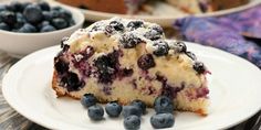 a piece of blueberry cake on a white plate with some blueberries around it