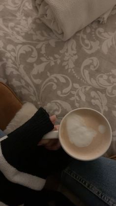 a person is holding a cup of coffee in their hand while sitting on a couch