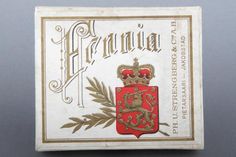 an old matchbox with a crest and crown on the front, sitting on a gray surface