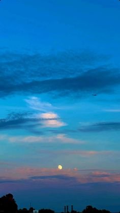 an airplane is flying in the sky at dusk with a full moon visible behind it