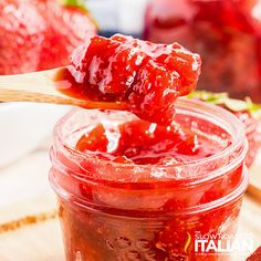 strawberry jam in a glass jar with a wooden spoon and strawberries on the side