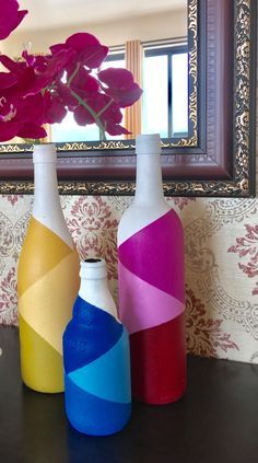 three colorful vases sitting on a table in front of a mirror