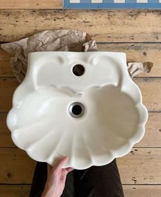 a white sink sitting on top of a wooden floor next to a hand holding it