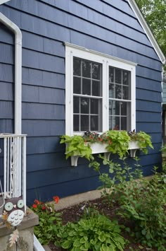 a blue house with white windows and flowers in the window boxes on the outside wall