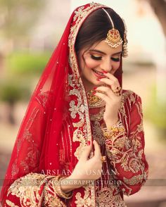 a woman in a red and gold bridal outfit with her hands to her mouth