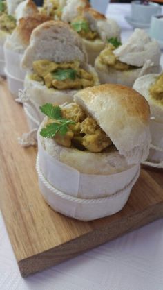 there are many small sandwiches on the wooden platter with green garnishes