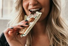 a woman holding a bar of chocolate in her hand and smiling at the camera while eating it