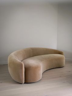 a curved couch sitting on top of a hard wood floor next to a white wall