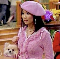 a woman in a pink dress and hat holding a small white dog on her lap