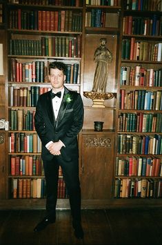 a man in a tuxedo standing in front of a bookcase