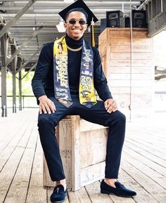 a man sitting on top of a wooden crate wearing a graduation cap and gown with his hands in his pockets