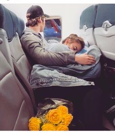 two people sleeping in the back seat of an airplane, with flowers on the floor