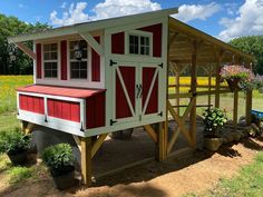 a small red and white chicken house in the middle of a field with yellow flowers