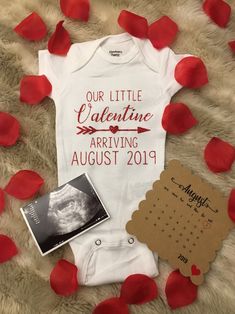 a baby's bodysuit and calendar are laying on a bed with rose petals