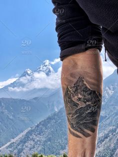 a man with a mountain tattoo on his leg is standing in front of the mountains