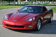 a red sports car parked on the side of a road in front of a cemetery