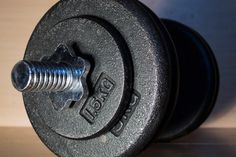 a pair of black dumbbells sitting on top of a wooden table next to a metal screw