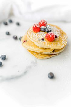 pancakes topped with berries and powdered sugar on a white tablecloth next to blueberries