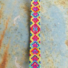 Brightly colored friendship bracelet in green, yellow, blue and hot pink colors, on rusty blue metallic surface. Handmade Multicolor Patterns For Festival, Bohemian Multicolor Patterns For Crafting, Multicolor Bohemian Patterns For Crafting, Knotted Jewelry, Making Friendship Bracelets, Diy Yarn, Yarn Craft, Small Pictures, Marzipan