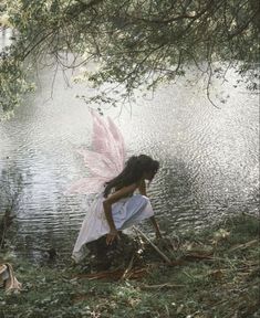 a woman in white dress standing next to a body of water with pink wings on it