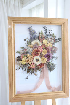 a bouquet of flowers in a wooden frame on a easel next to a window