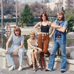 three women and one man are posing for a photo in front of a pond with palm trees