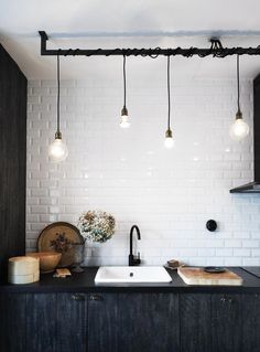 a kitchen with white brick walls and black counter tops, hanging lights above the sink