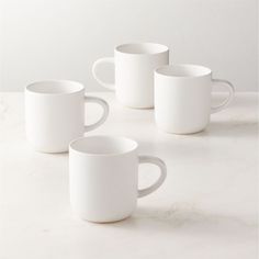 four white coffee mugs sitting on top of a marble countertop next to each other