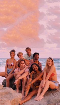 a group of young people sitting on top of rocks near the ocean at sunset or dawn