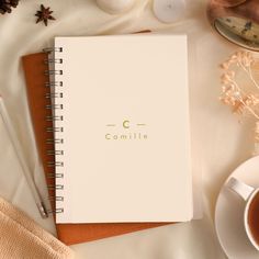 a white notebook sitting on top of a table next to a cup of coffee