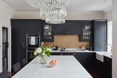 a kitchen with black cabinets and white counter tops, chandelier above the island