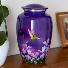 a purple vase sitting on top of a wooden table next to a potted plant