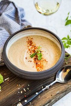 a bowl filled with soup next to a spoon and glass of wine on a wooden table